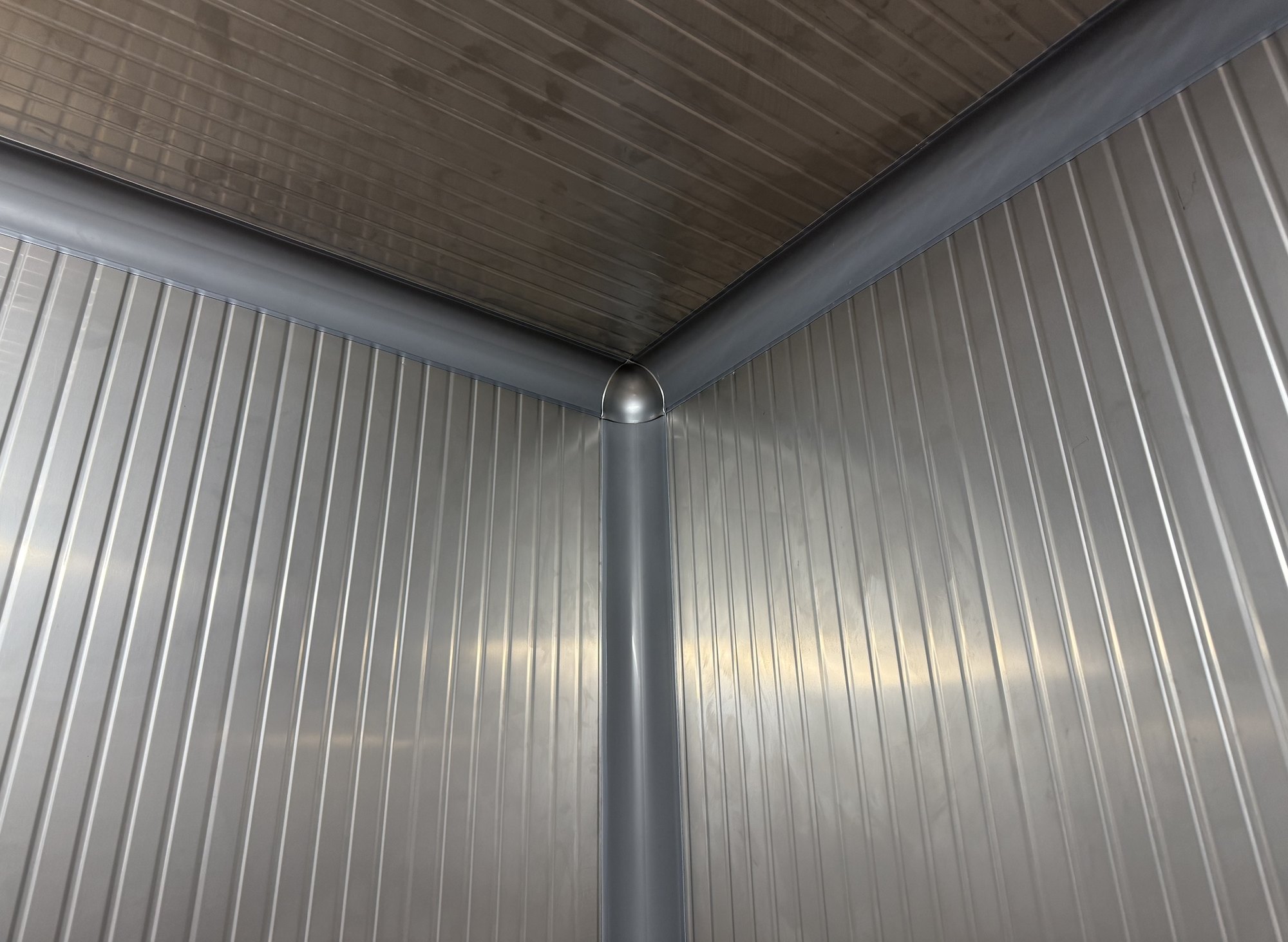 Close-up of a CoRound Basic PVC 3-way corner piece in Stainless Steel Gray 9023 joining three coves where two walls of stainless steel panels meet the ceiling